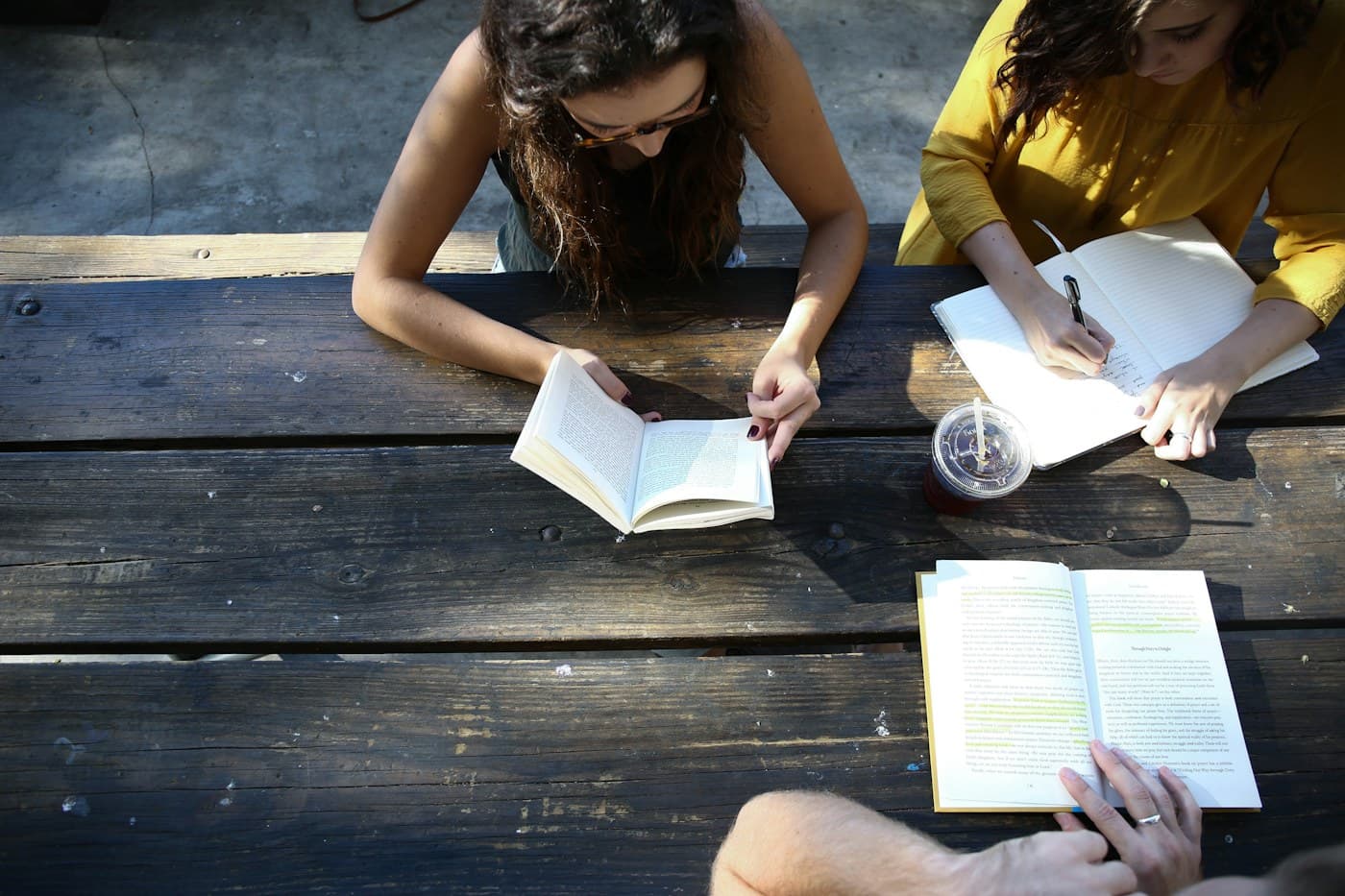 People reading, writing, and sharing a table in the sunlight.